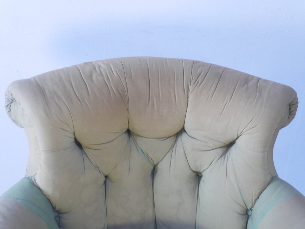 A 19th-century Victorian armchair upholstered in olive fabric with a button-backed scroll back, turned timber front legs on brass castors, and a fitted seat cushion. View X