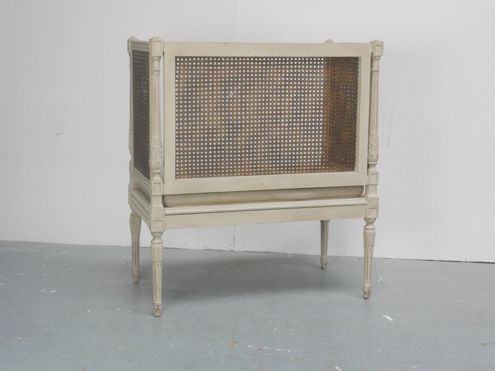 A painted off-white neoclassical window seat featuring high woven cane side and back panels, turned fluted legs, and a fitted cream cushion. View III