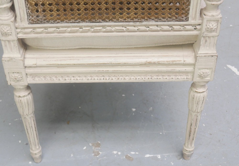 A painted off-white neoclassical window seat featuring high woven cane side and back panels, turned fluted legs, and a fitted cream cushion. View V