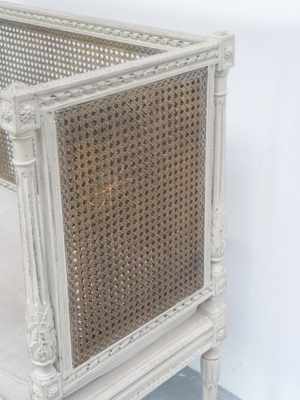 A painted off-white neoclassical window seat featuring high woven cane side and back panels, turned fluted legs, and a fitted cream cushion. View VIII
