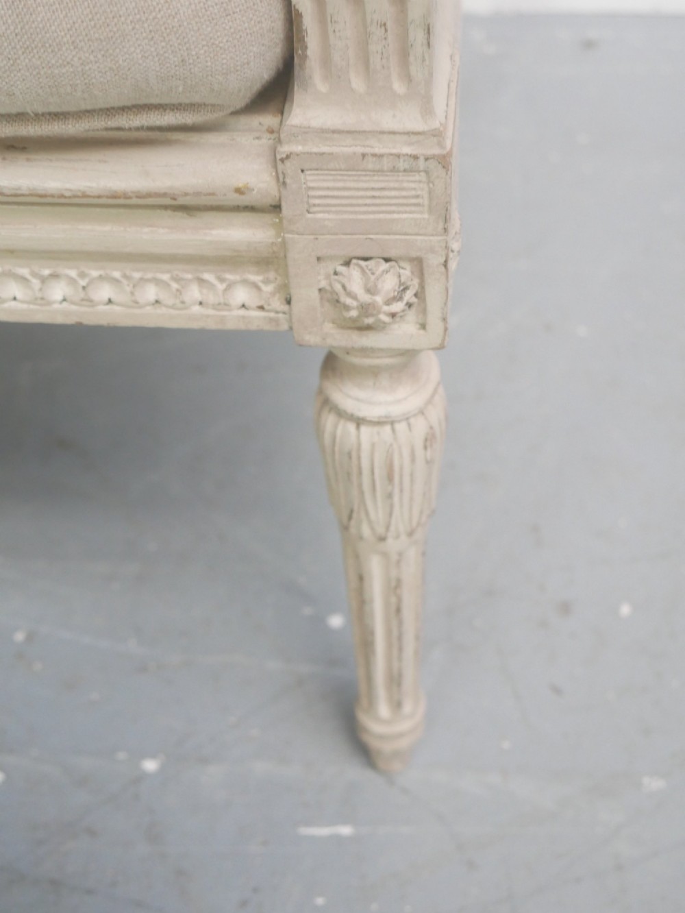 A painted off-white neoclassical window seat featuring high woven cane side and back panels, turned fluted legs, and a fitted cream cushion. View XII