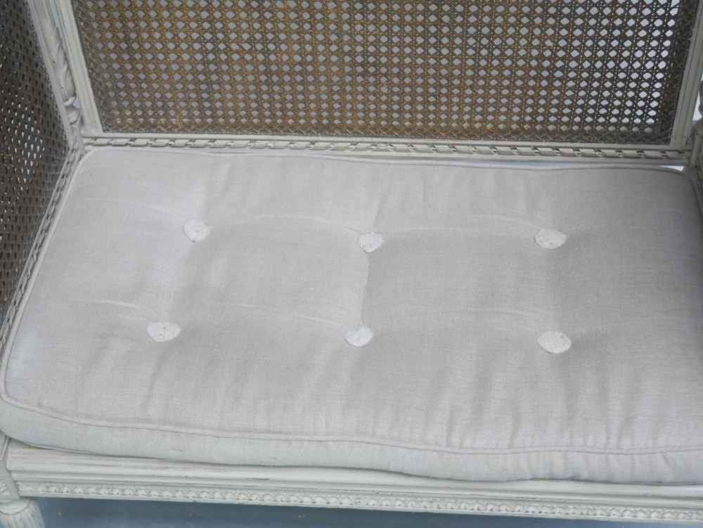 A painted off-white neoclassical window seat featuring high woven cane side and back panels, turned fluted legs, and a fitted cream cushion. View XIII