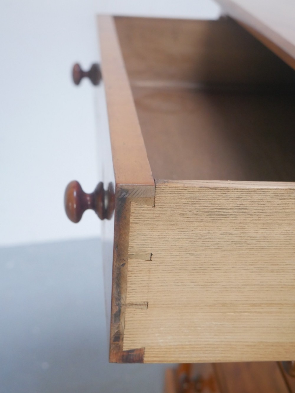 An antique Scottish wooden chest featuring four full-width drawers with dark turned handles and carved roundel details at the upper corners. View III