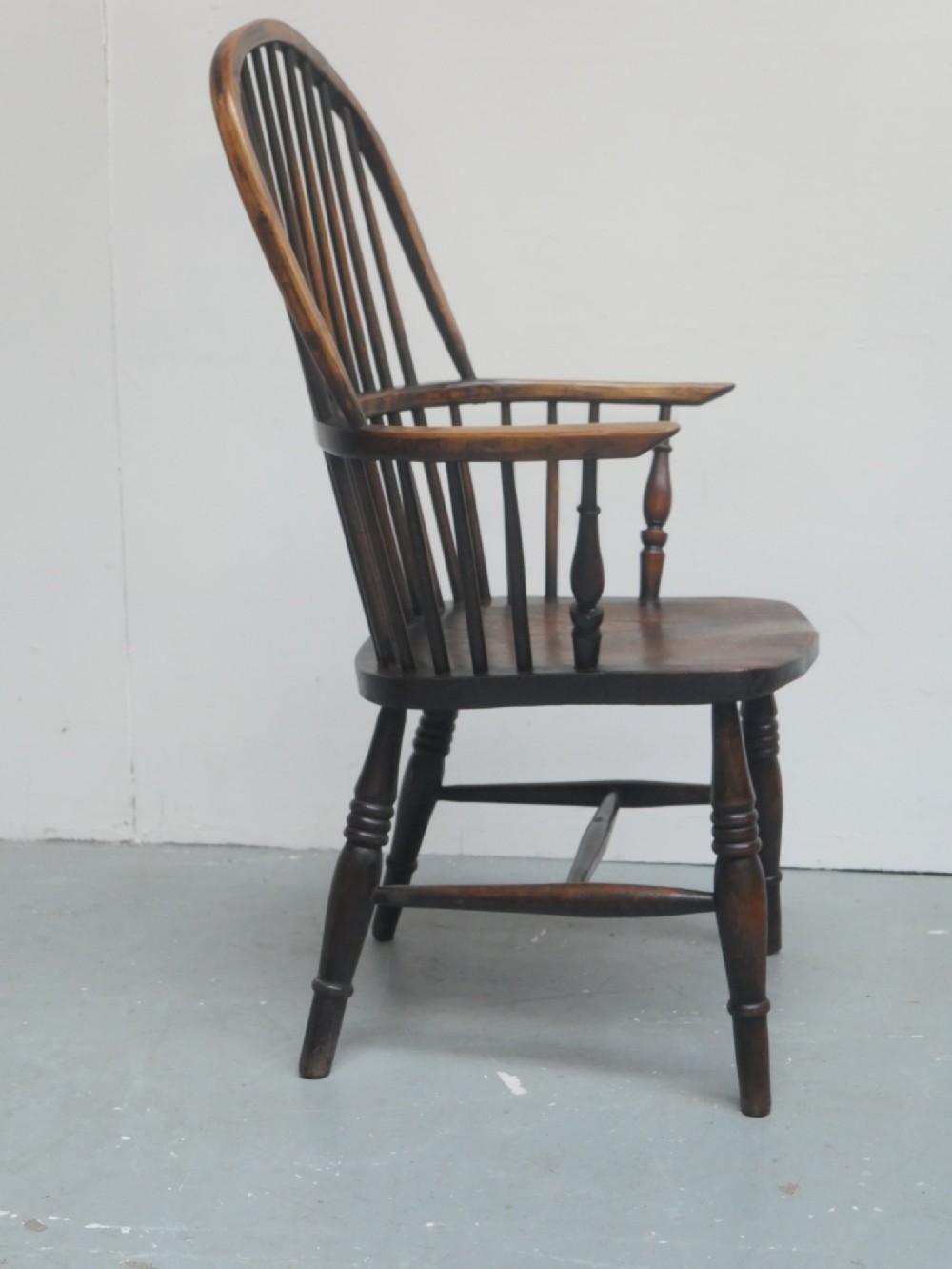 A dark brown wooden Windsor armchair featuring a rounded hoop back, vertical spindles, turned legs, and an H-stretcher. View III