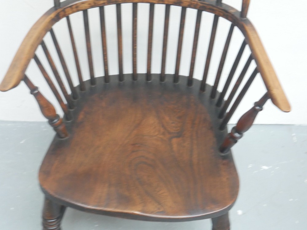 A dark brown wooden Windsor armchair featuring a rounded hoop back, vertical spindles, turned legs, and an H-stretcher. View V