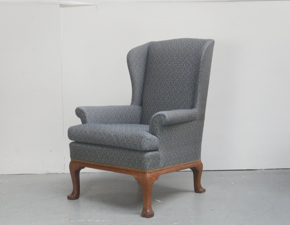 A Scottish wingback armchair upholstered in patterned slate blue fabric featuring mahogany cabriole front legs and brass stud detailing along the lower frame.