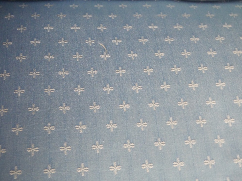 A light blue patterned fabric Chesterfield sofa featuring deep buttoning across the backrest and rolled arms, supported by turned wooden legs on brass castors. View III