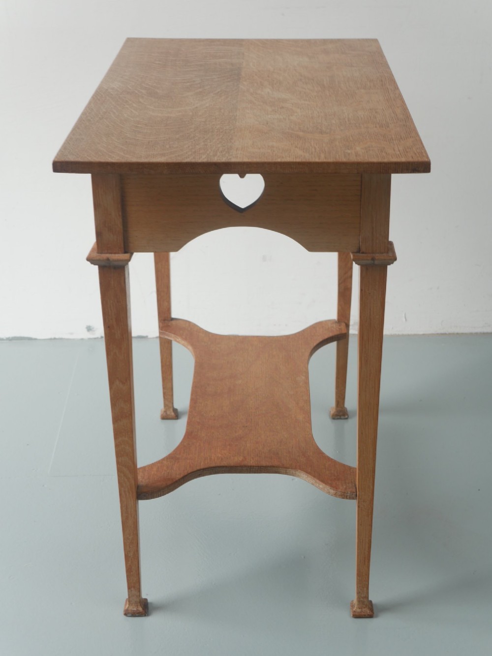 An Arts and Crafts oak lamp table featuring heart cut-out details on the apron, tapered square legs, and a contoured undertier shelf. View VI