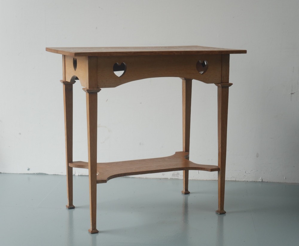 An Arts and Crafts oak lamp table featuring heart cut-out details on the apron, tapered square legs, and a contoured undertier shelf. View VII
