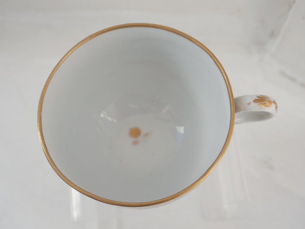 An antique porcelain teacup and matching saucer featuring cobalt blue borders with gold foliate motifs and central monochrome pastoral scenes. View VIII