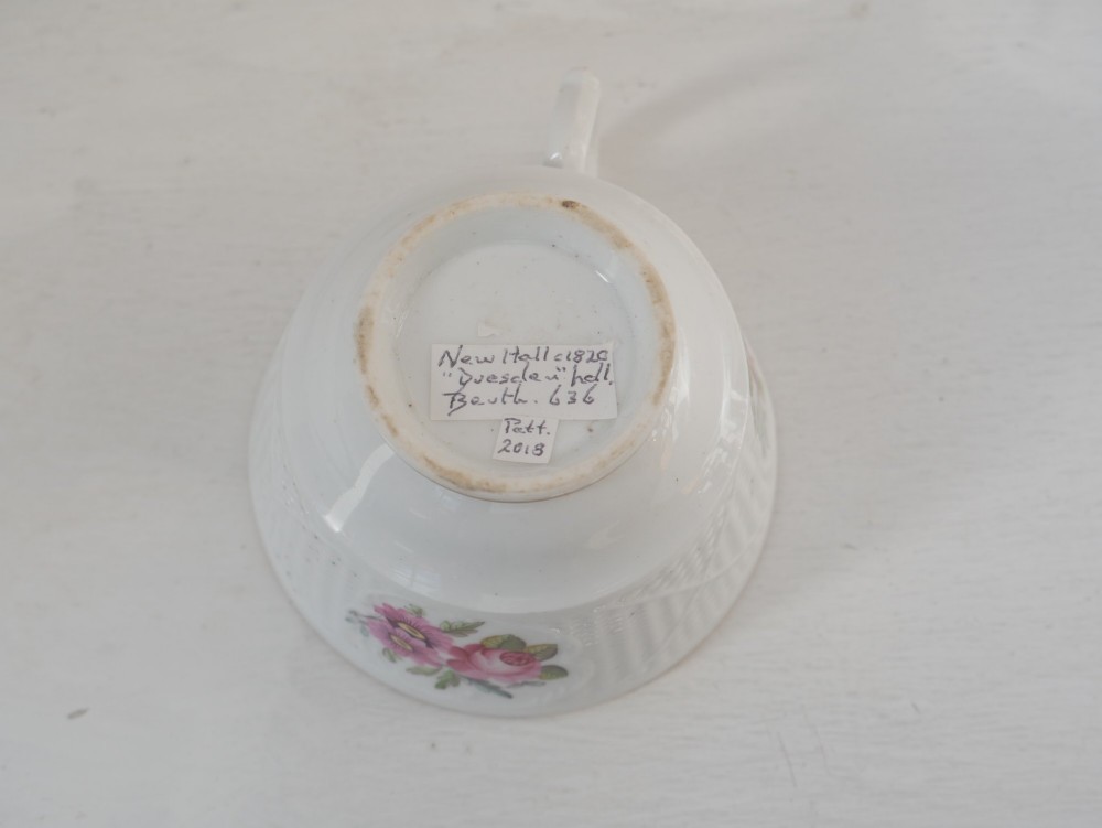 An antique white porcelain teacup and matching saucer featuring hand-painted floral sprays, moulded textured borders, and gilded rim details. View III