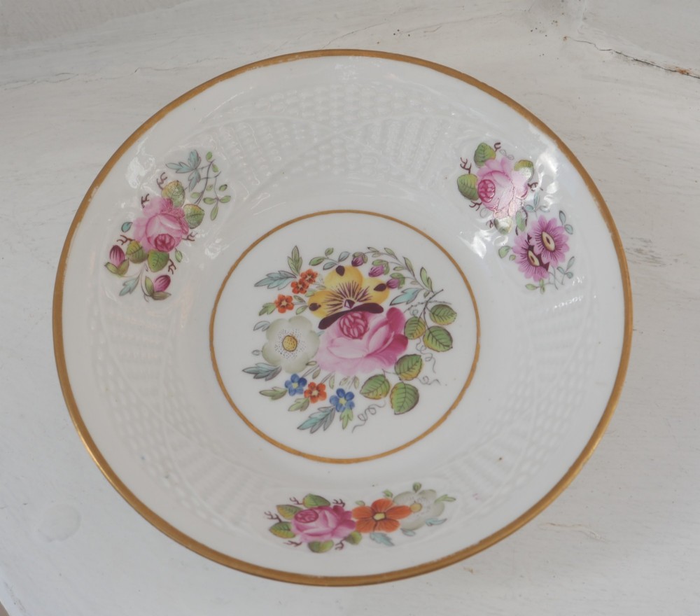 An antique white porcelain teacup and matching saucer featuring hand-painted floral sprays, moulded textured borders, and gilded rim details. View VI