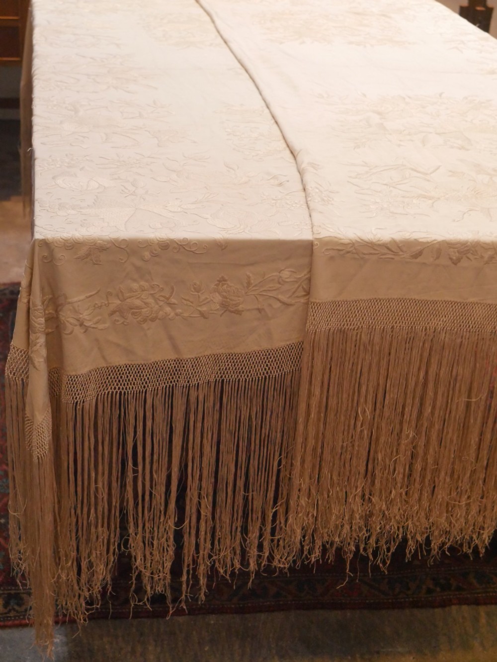 A cream-coloured silk piano shawl featuring tonal floral hand embroidery and deep knotted fringe edge. View II