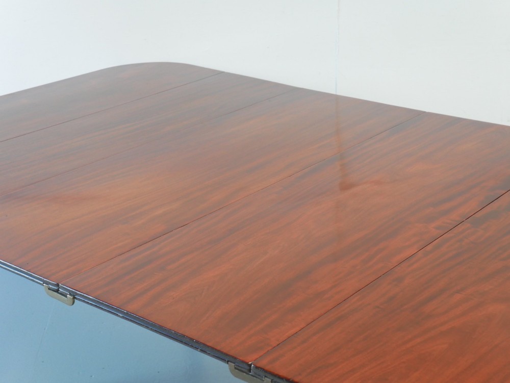 A large antique Regency mahogany extending dining table featuring rounded corners, removable leaves, and reeded legs with brass castors. View II