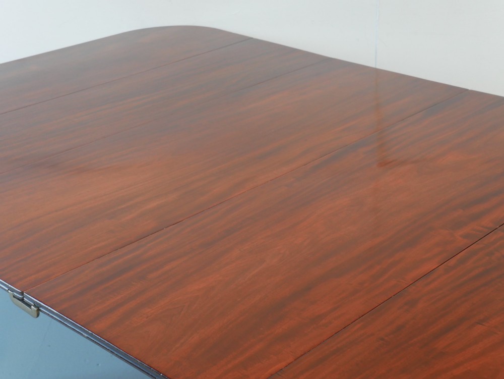 A large antique Regency mahogany extending dining table featuring rounded corners, removable leaves, and reeded legs with brass castors. View III