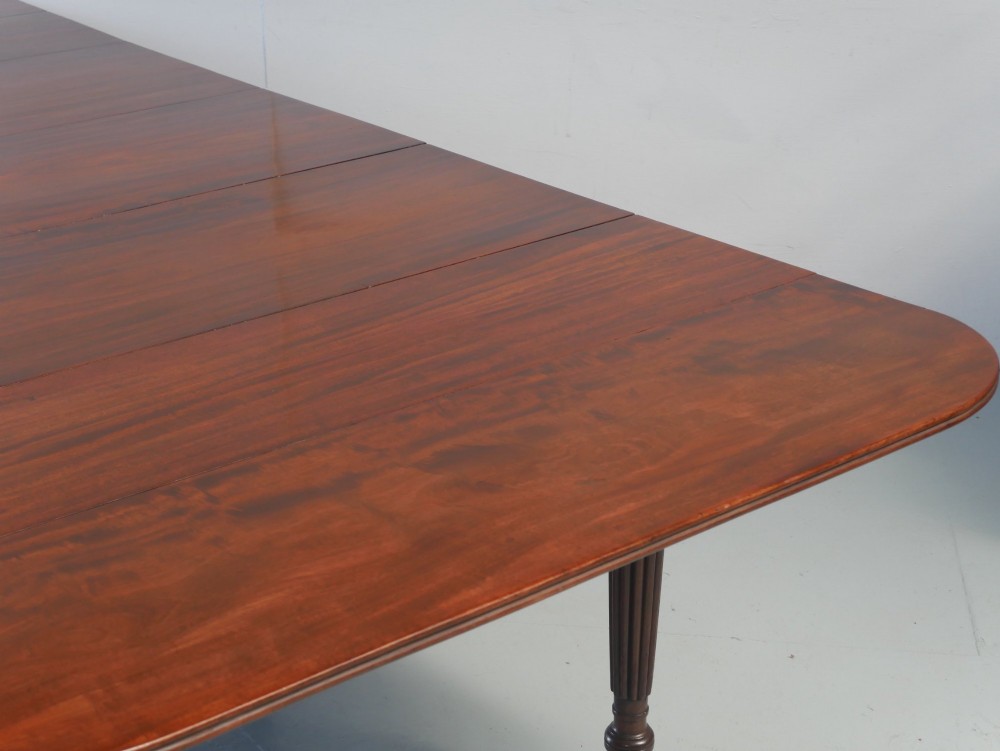 A large antique Regency mahogany extending dining table featuring rounded corners, removable leaves, and reeded legs with brass castors. View IV