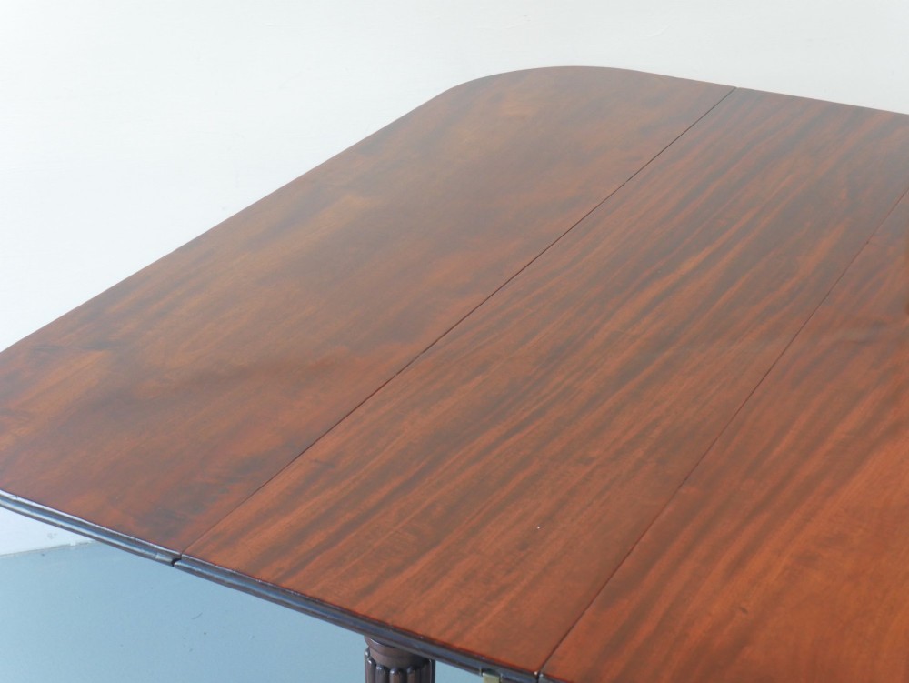 A large antique Regency mahogany extending dining table featuring rounded corners, removable leaves, and reeded legs with brass castors. View V