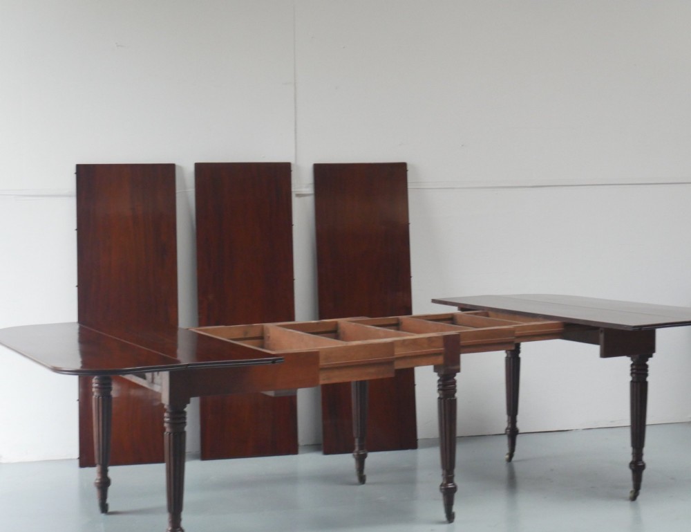 A large antique Regency mahogany extending dining table featuring rounded corners, removable leaves, and reeded legs with brass castors. View VI