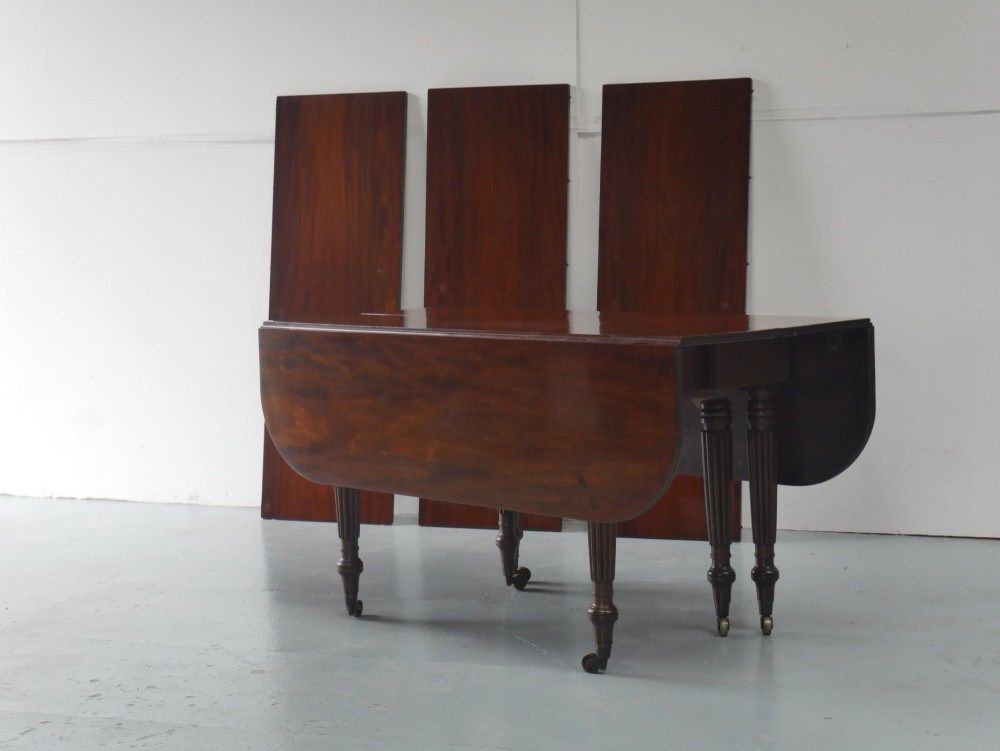 A large antique Regency mahogany extending dining table featuring rounded corners, removable leaves, and reeded legs with brass castors. View VII