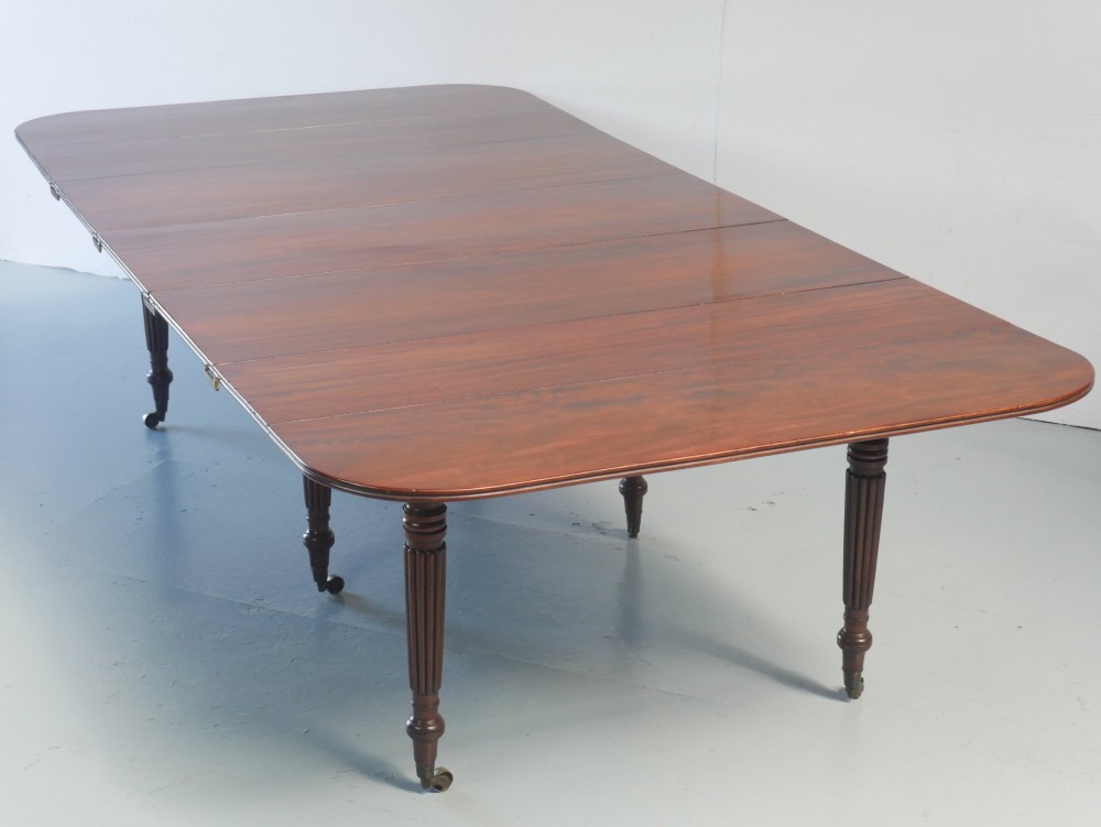 A large antique Regency mahogany extending dining table featuring rounded corners, removable leaves, and reeded legs with brass castors. View XI