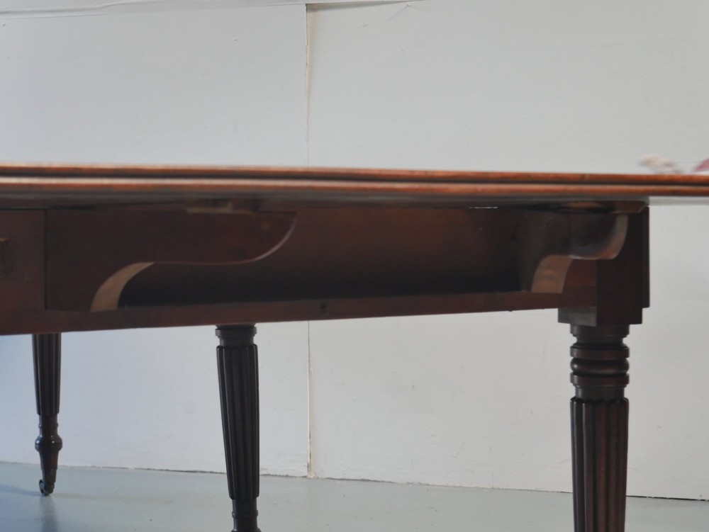 A large antique Regency mahogany extending dining table featuring rounded corners, removable leaves, and reeded legs with brass castors. View XII