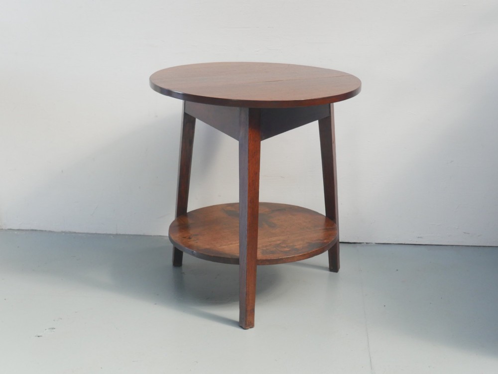 An antique oak cricket table featuring a circular top, three splayed legs, a triangular apron, and a lower circular undertier.