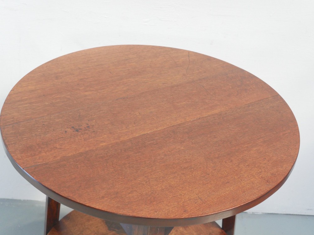 An antique oak cricket table featuring a circular top, three splayed legs, a triangular apron, and a lower circular undertier. View II