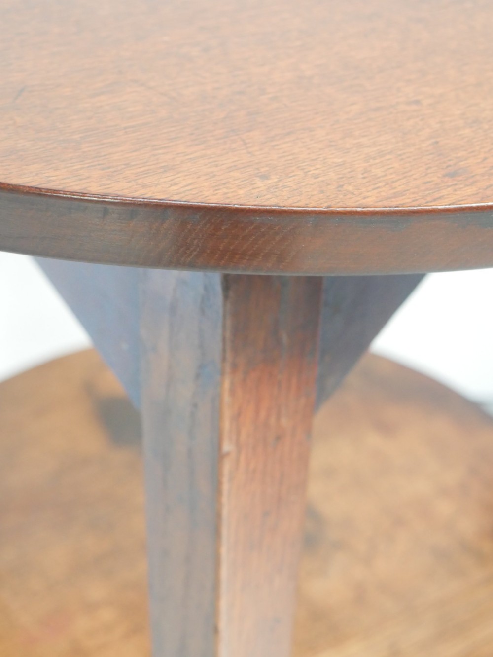 An antique oak cricket table featuring a circular top, three splayed legs, a triangular apron, and a lower circular undertier. View III