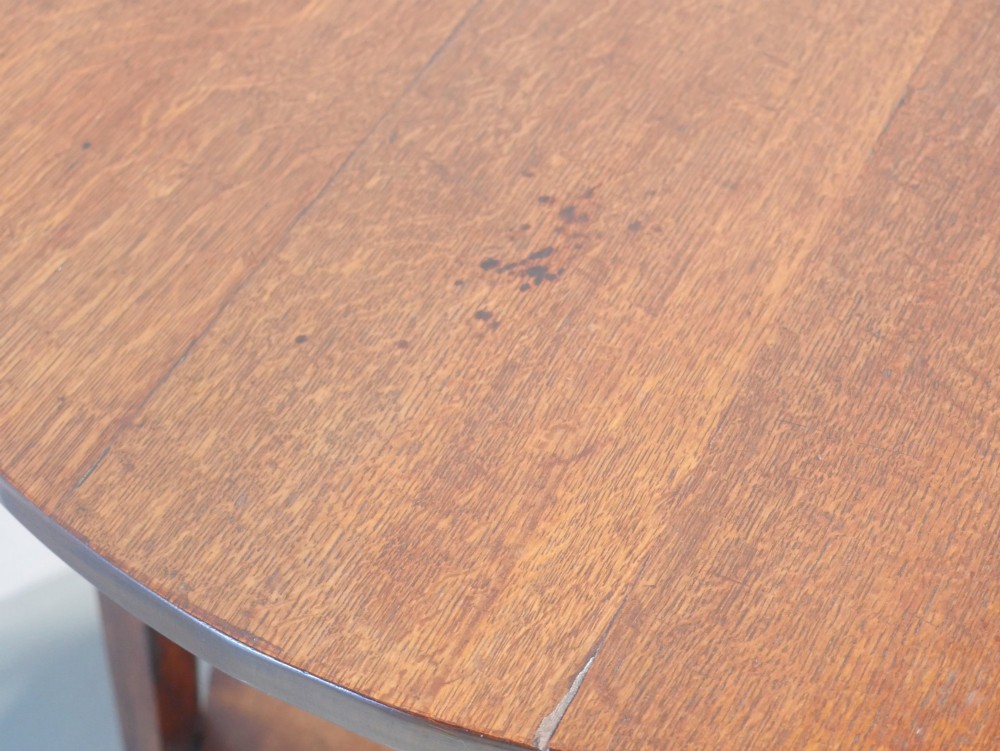 An antique oak cricket table featuring a circular top, three splayed legs, a triangular apron, and a lower circular undertier. View VII
