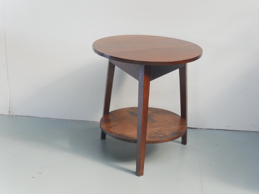 An antique oak cricket table featuring a circular top, three splayed legs, a triangular apron, and a lower circular undertier. View IX
