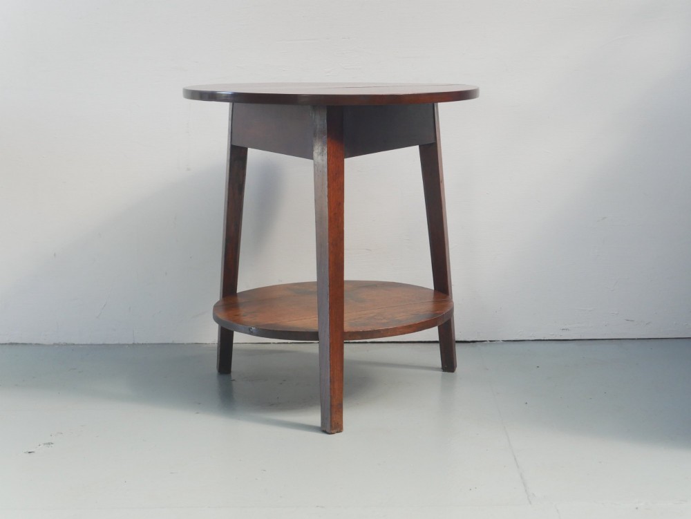 An antique oak cricket table featuring a circular top, three splayed legs, a triangular apron, and a lower circular undertier. View X