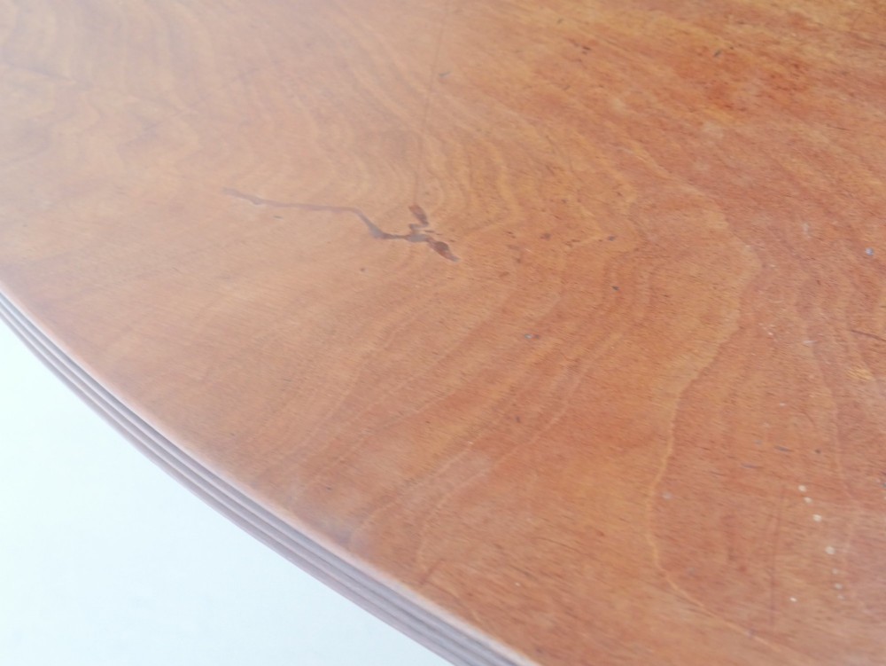 An antique Regency oval mahogany tilt-top table shown upright on a splayed pedestal base with brass castors. View VI