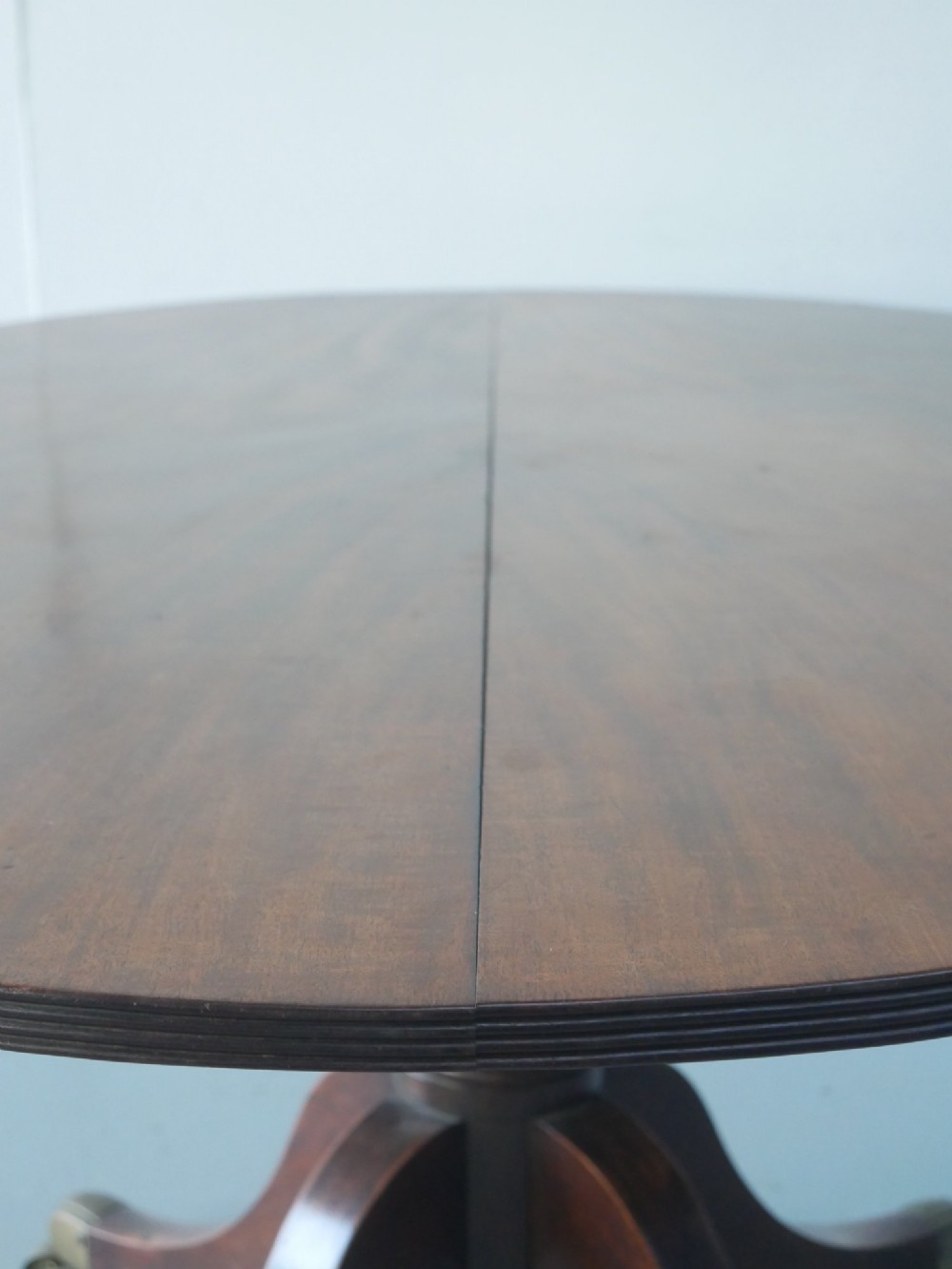 An antique Regency oval mahogany tilt-top table shown upright on a splayed pedestal base with brass castors. View VIII