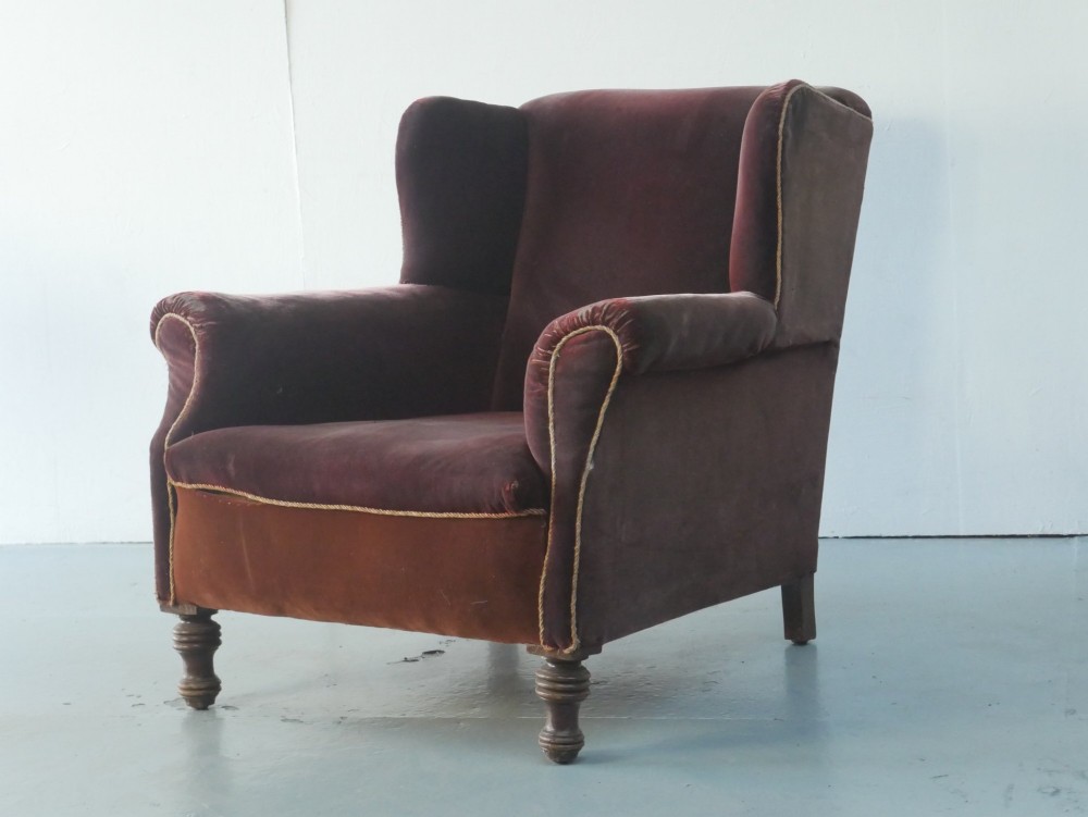 A high-backed antique wing armchair upholstered in deep burgundy velvet with corded piping details and turned wood front legs.