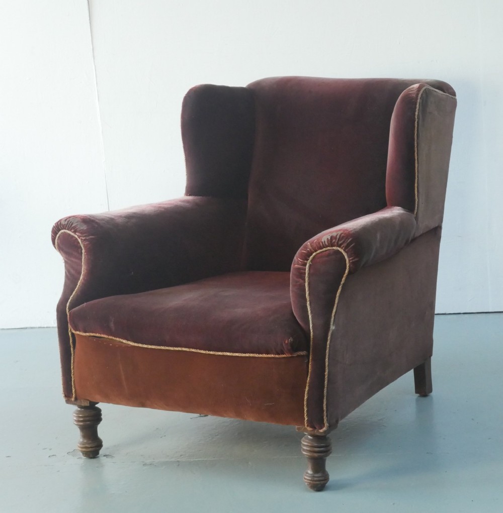A high-backed antique wing armchair upholstered in deep burgundy velvet with corded piping details and turned wood front legs. View II