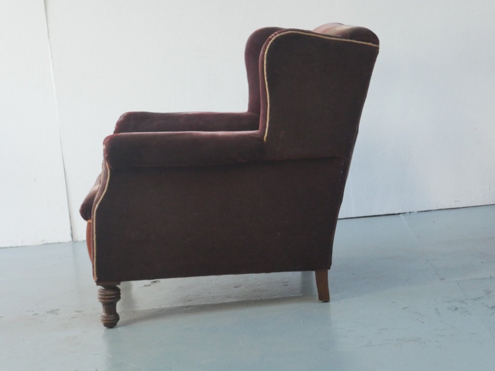 A high-backed antique wing armchair upholstered in deep burgundy velvet with corded piping details and turned wood front legs. View IV