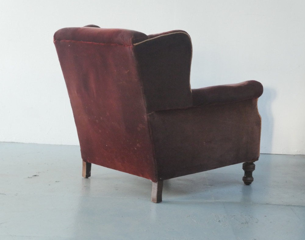 A high-backed antique wing armchair upholstered in deep burgundy velvet with corded piping details and turned wood front legs. View V