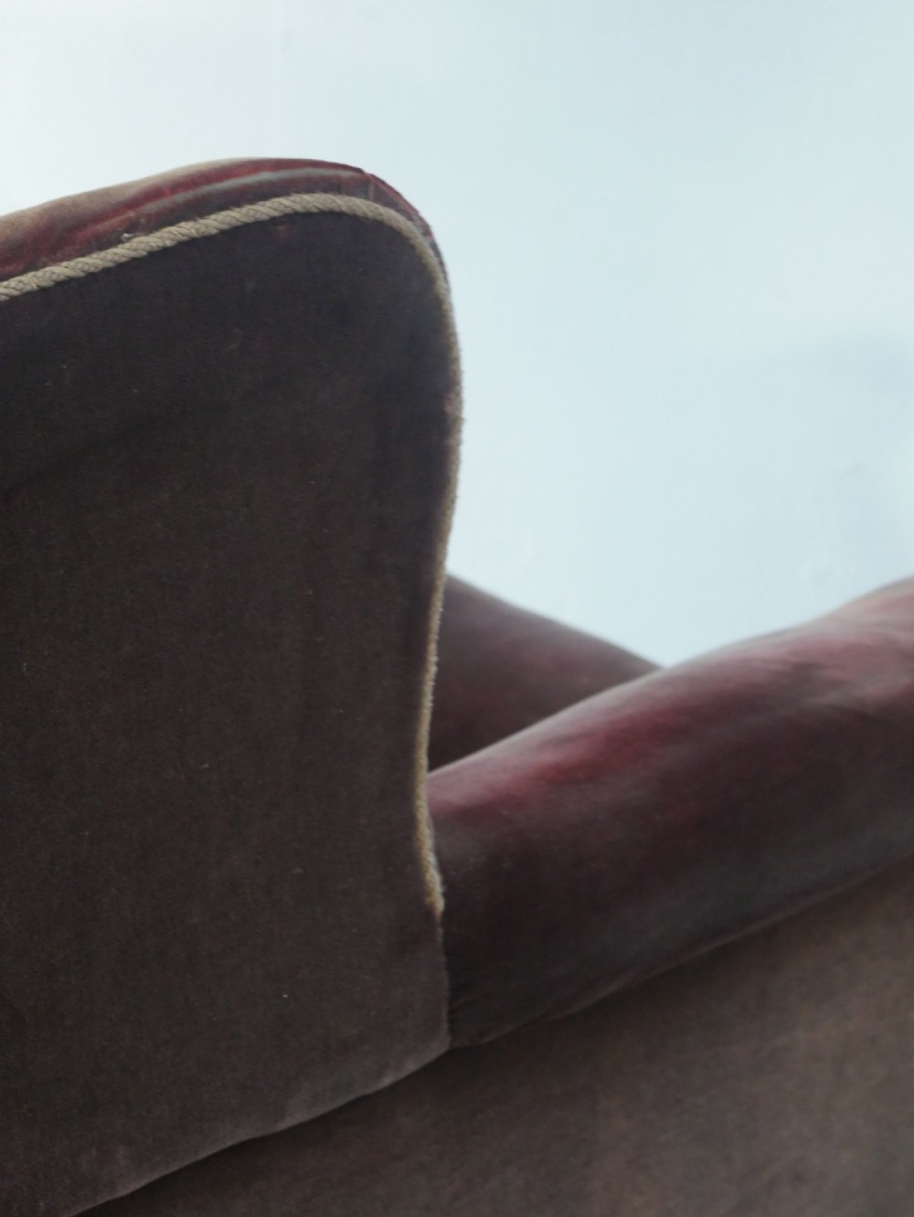 A high-backed antique wing armchair upholstered in deep burgundy velvet with corded piping details and turned wood front legs. View VI