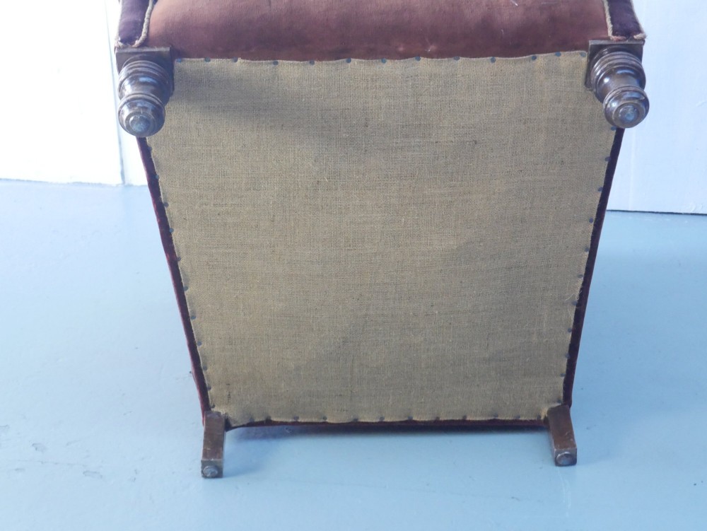 A high-backed antique wing armchair upholstered in deep burgundy velvet with corded piping details and turned wood front legs. View VII