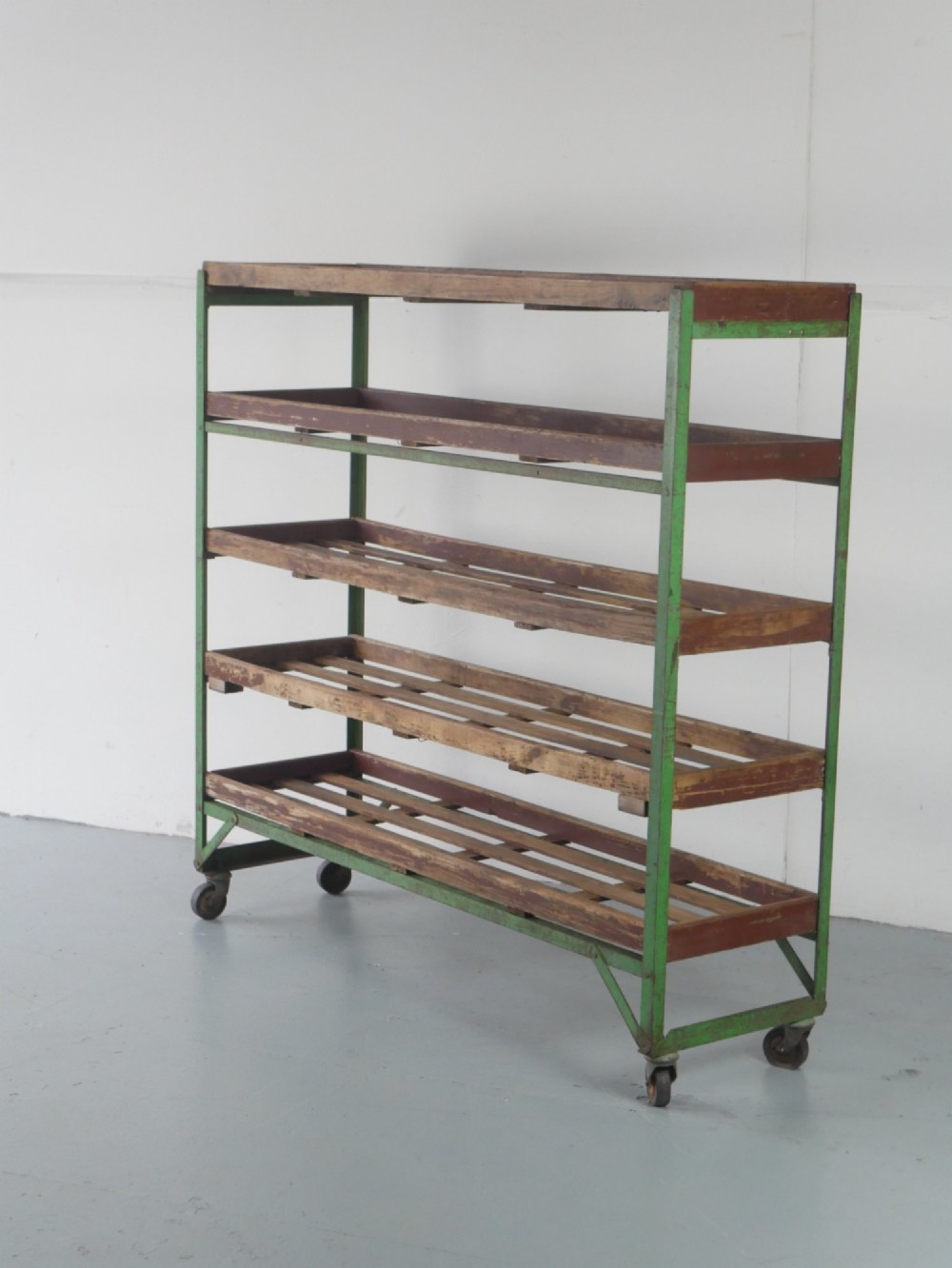 An industrial multi-tiered storage rack featuring slatted wooden shelves within a green painted metal frame fitted with castors.