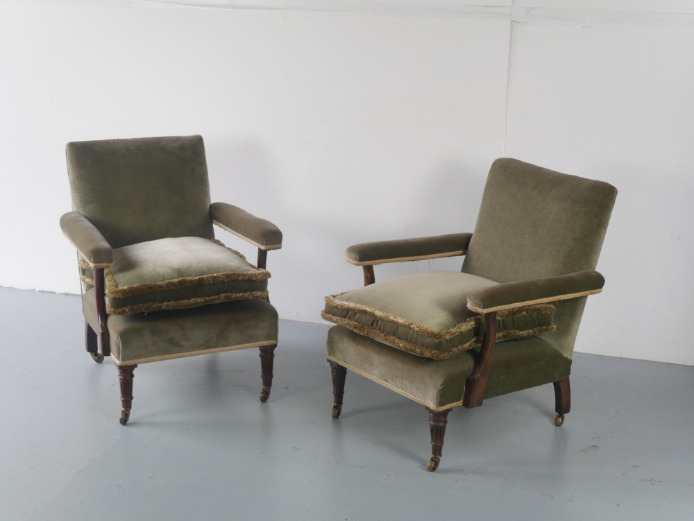 A matched pair of armchairs upholstered in olive green velvet with fringed seat cushions and turned front legs on brass castors.