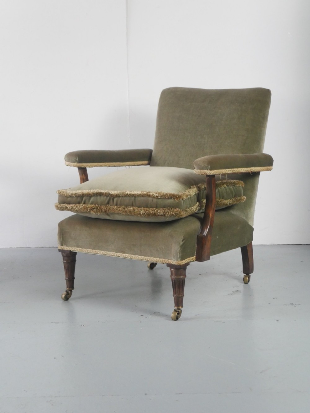 A matched pair of armchairs upholstered in olive green velvet with fringed seat cushions and turned front legs on brass castors. View II