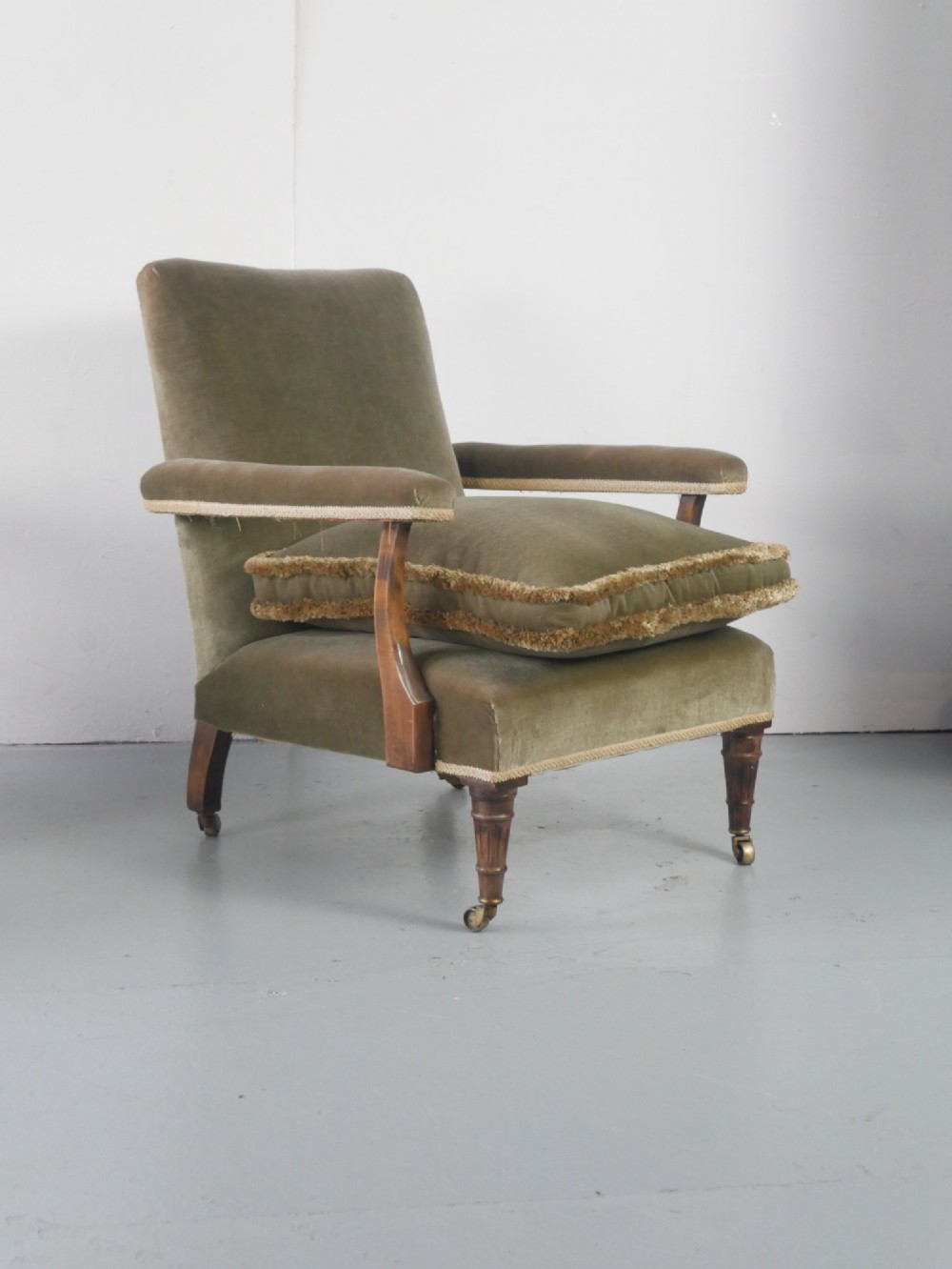 A matched pair of armchairs upholstered in olive green velvet with fringed seat cushions and turned front legs on brass castors. View IV