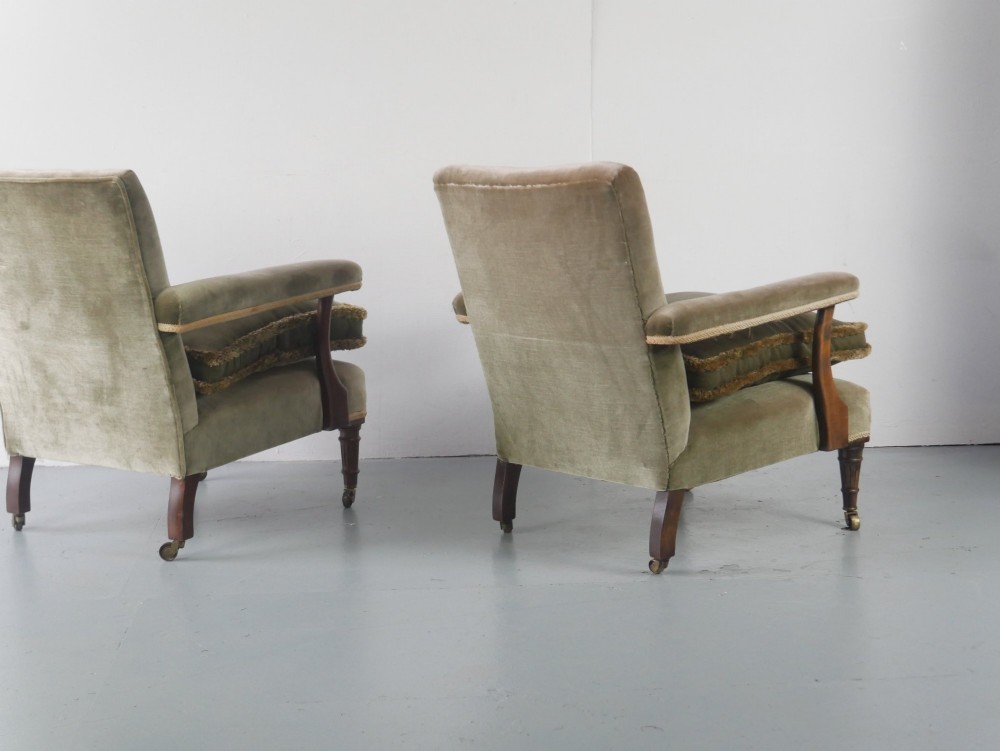 A matched pair of armchairs upholstered in olive green velvet with fringed seat cushions and turned front legs on brass castors. View V