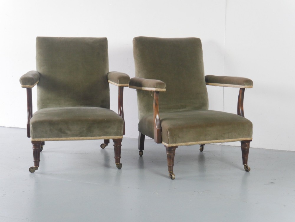 A matched pair of armchairs upholstered in olive green velvet with fringed seat cushions and turned front legs on brass castors. View X