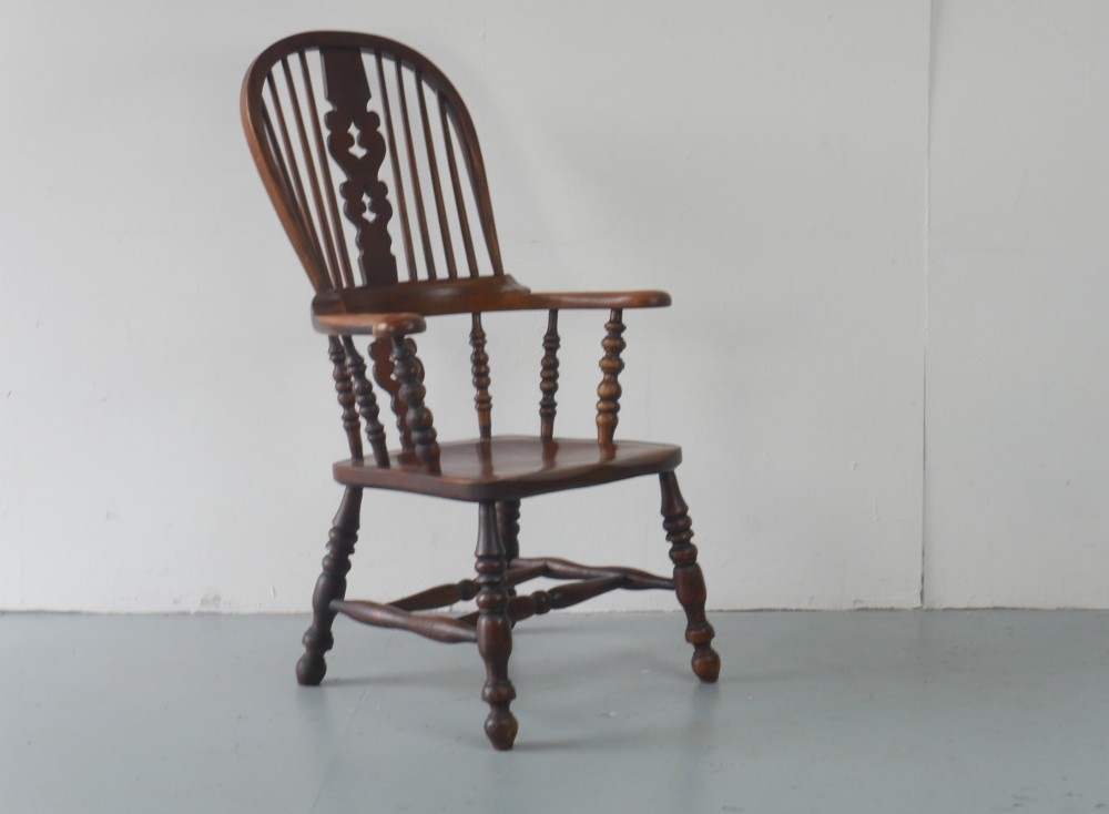 A wooden broad-arm Windsor armchair featuring a hoop back, pierced central splat, turned spindles, and a saddle seat.