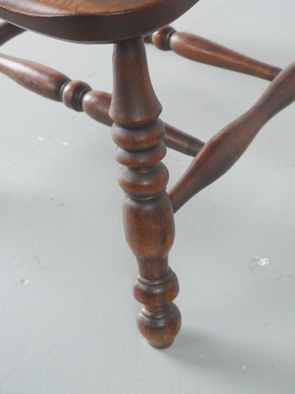 A wooden broad-arm Windsor armchair featuring a hoop back, pierced central splat, turned spindles, and a saddle seat. View V