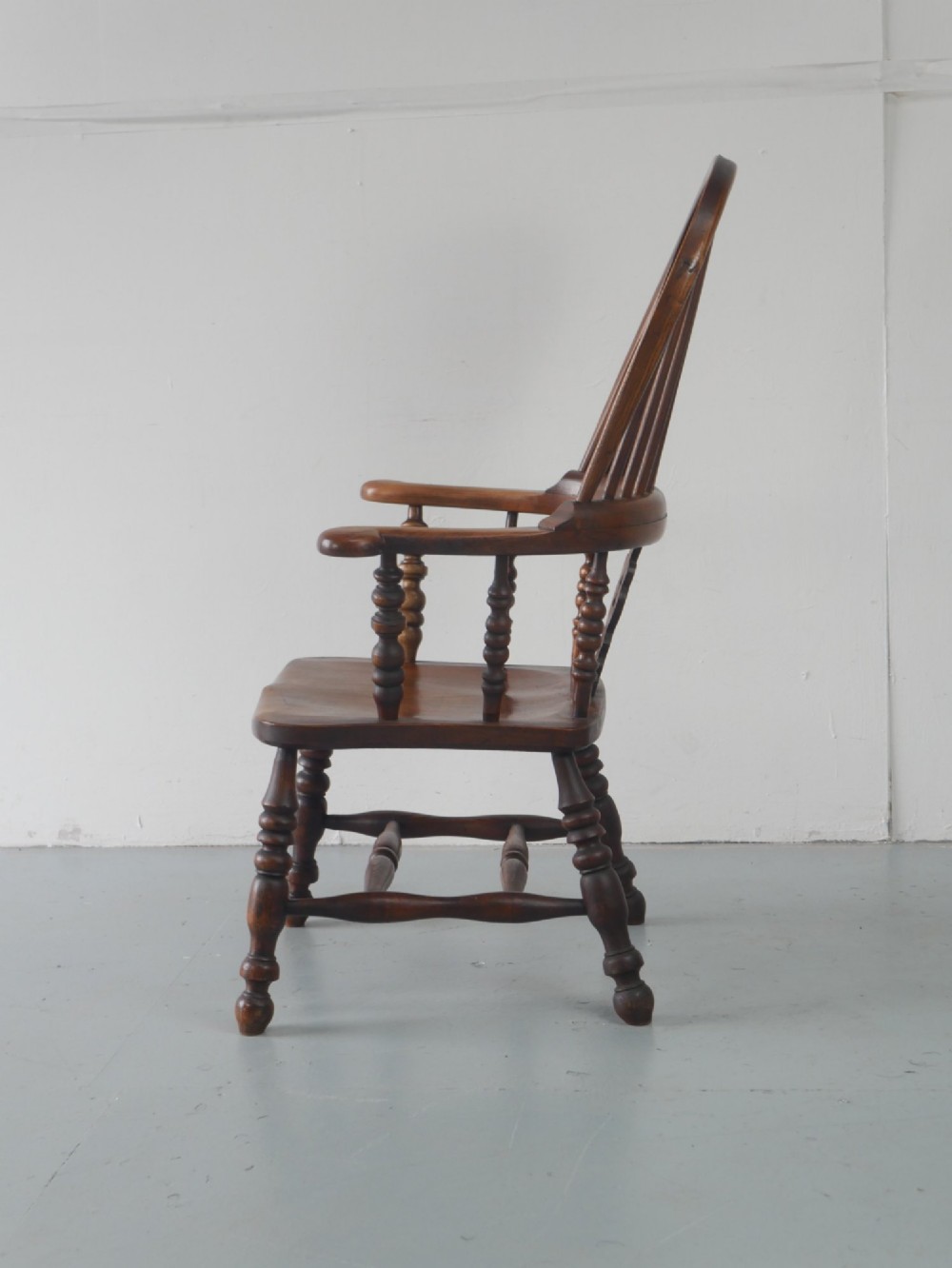 A wooden broad-arm Windsor armchair featuring a hoop back, pierced central splat, turned spindles, and a saddle seat. View VI