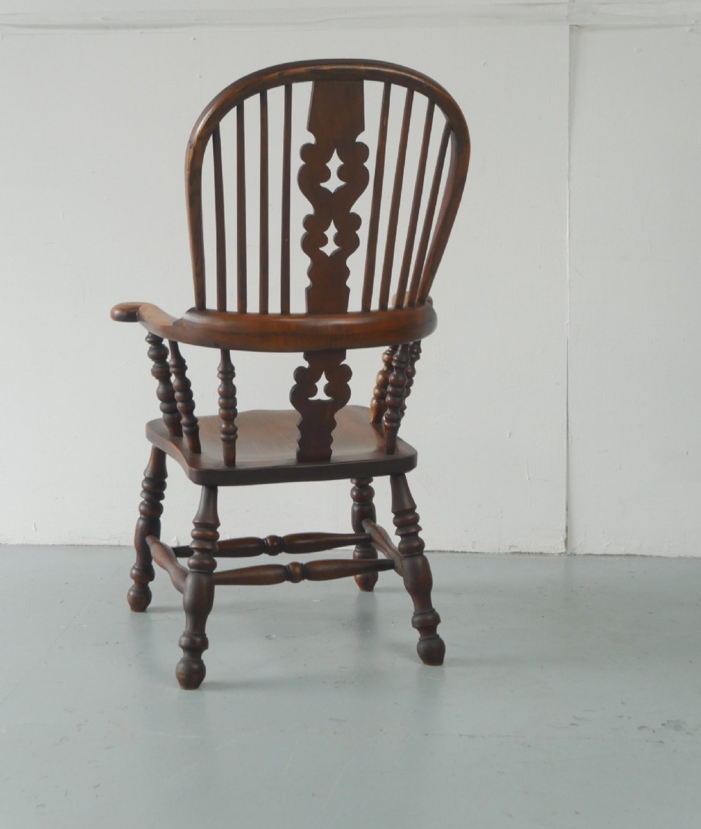 A wooden broad-arm Windsor armchair featuring a hoop back, pierced central splat, turned spindles, and a saddle seat. View IX