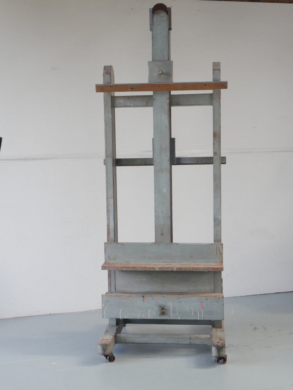 A large floor-standing double-sided timber studio easel with a distressed grey finish, adjustable height mechanism, and metal castor feet. View II